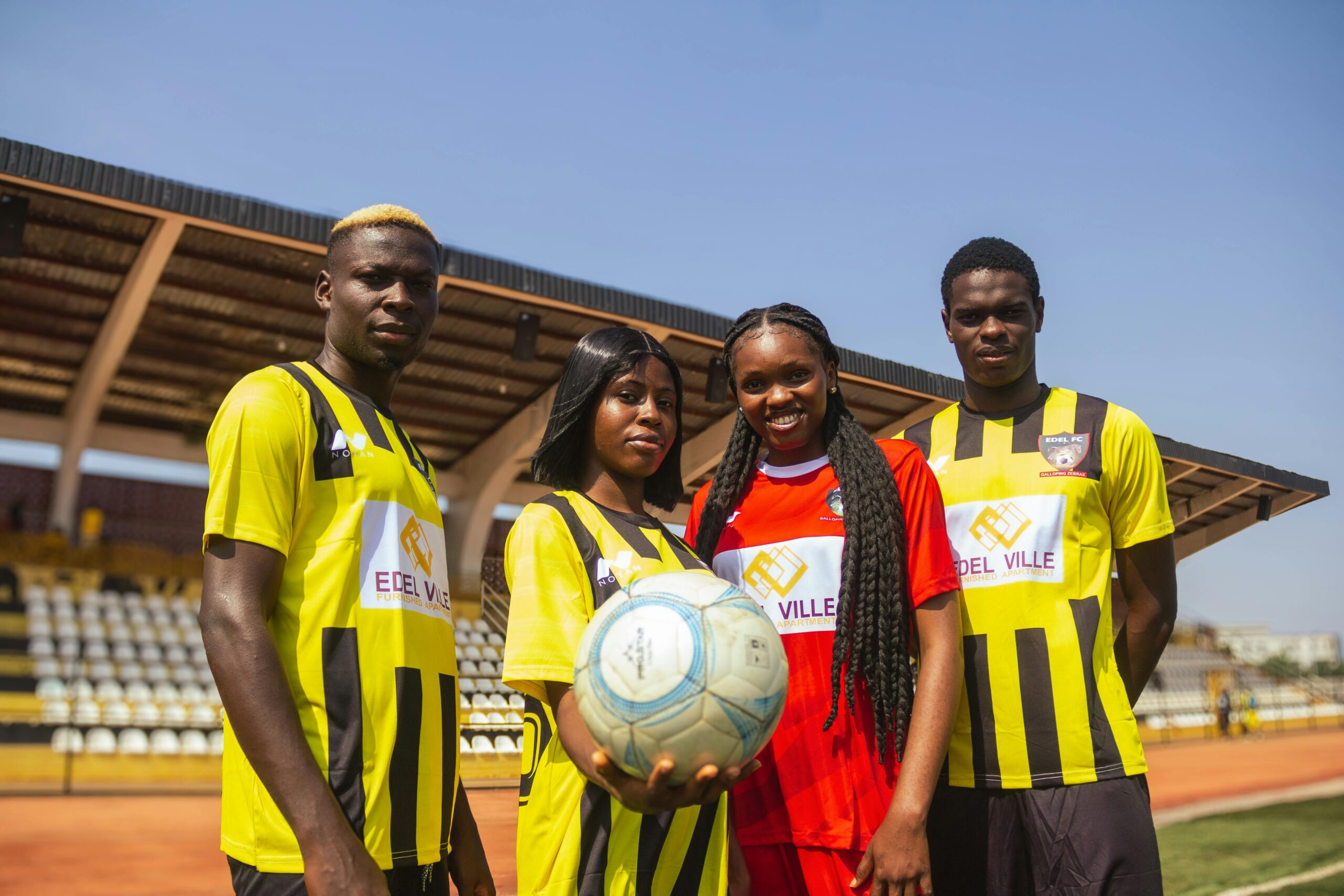 Group of young African football players posing on a sunny day in a stadium.